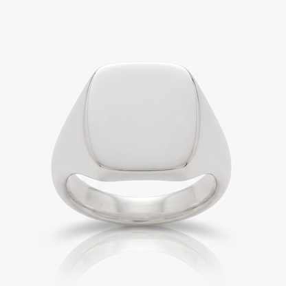 A polished silver signet ring with a smooth, rounded square face, shown on a clean white background with a soft reflection below.

